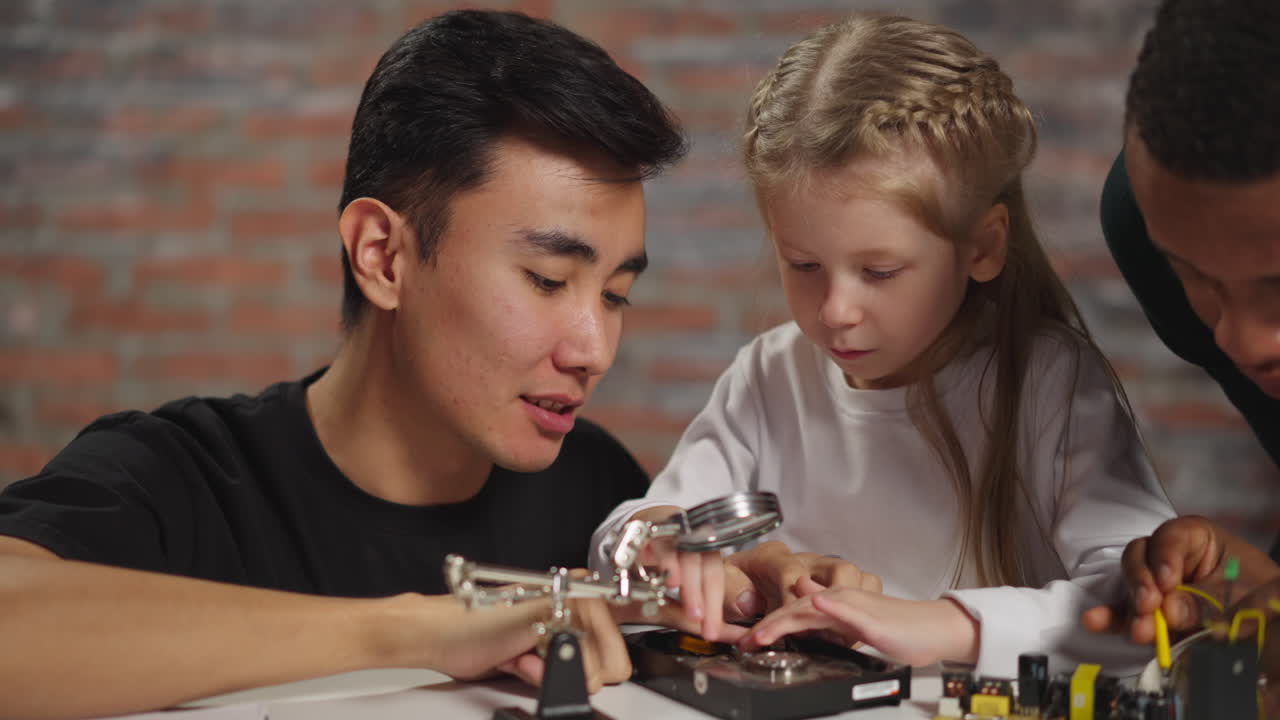 un ingeniero asiático muestra un disco duro abierto a un estudiante curioso.