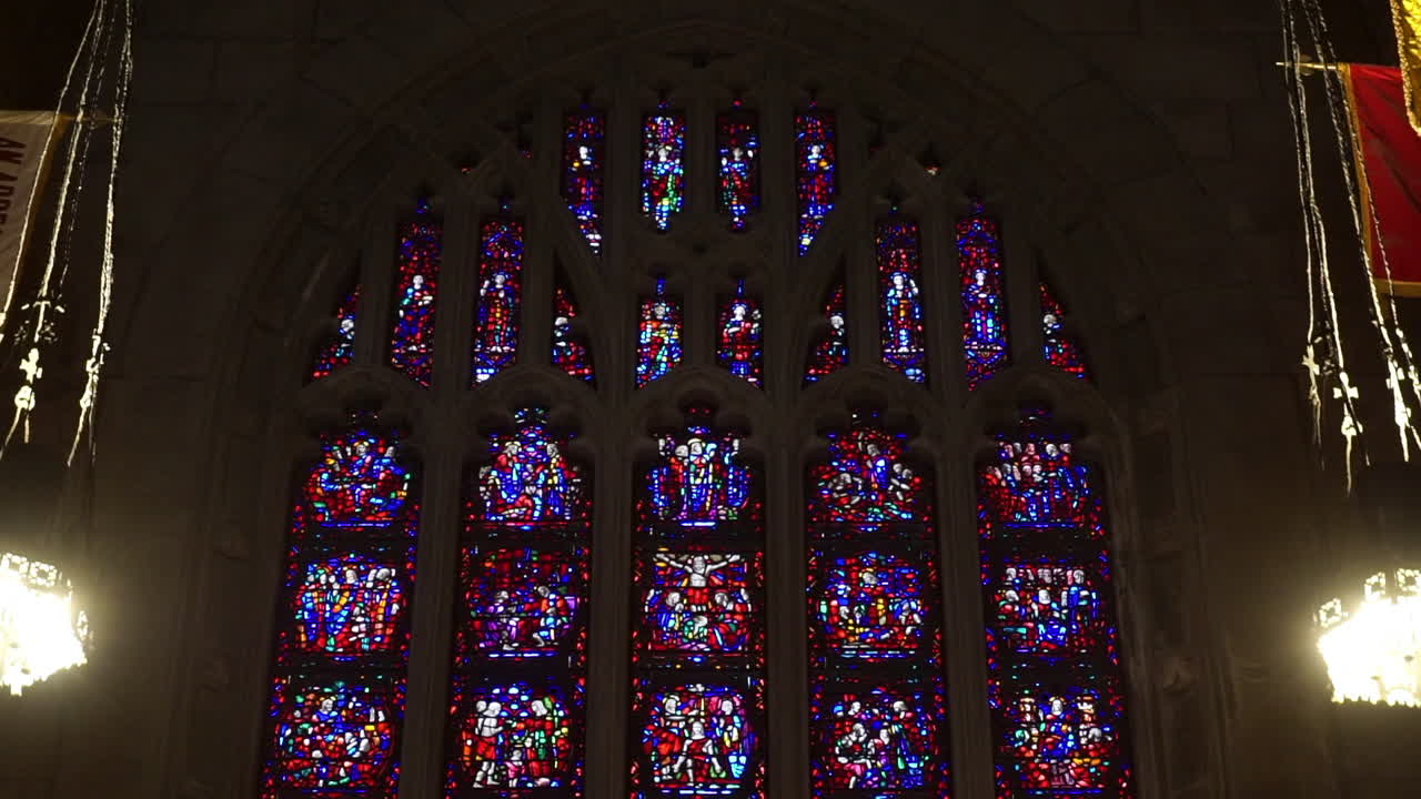 Stained glass gothic window between lamps and banners inside cathedral