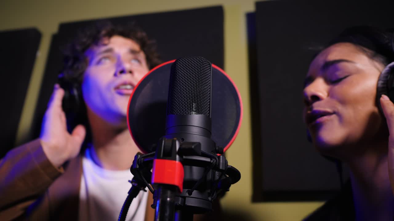 dos jóvenes cantantes interpretando su canción en un estudio de grabación. dúo de músicos profesionales grabando un nuevo álbum cd. hermosa pareja trabajando juntos. cámara lenta. 4k