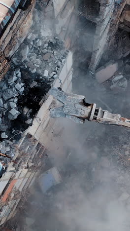 aerial view excavators dismantle the concrete structures of the building. hydraulic machinery working to get rid of the rubbish in a demolition site. vertical video