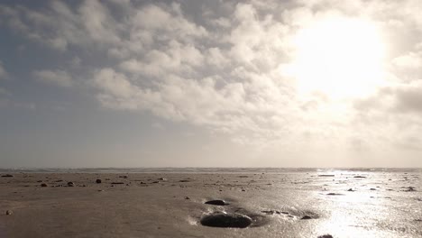 Niedriger-Winkel,-Ozeanstrandsand-Mit-Kieseln,-Kleinen-Wellen-Und-Wolken