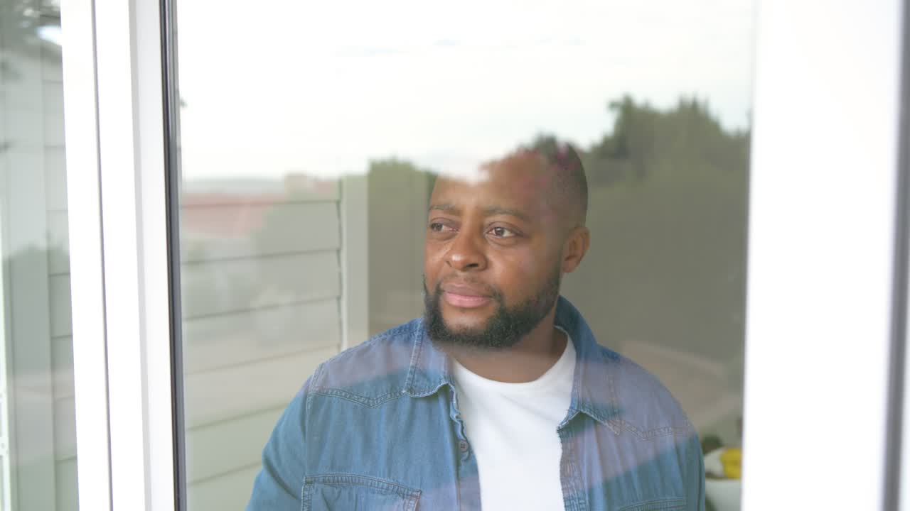 Man in his 30s standing by sliding door gazing outside taking glass drinking walking away