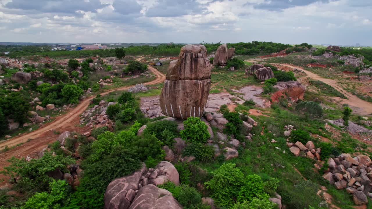 Granite hill with trees, sand road way and rainy clouds at telangana, india. day time, push in, drone shot, 4k.