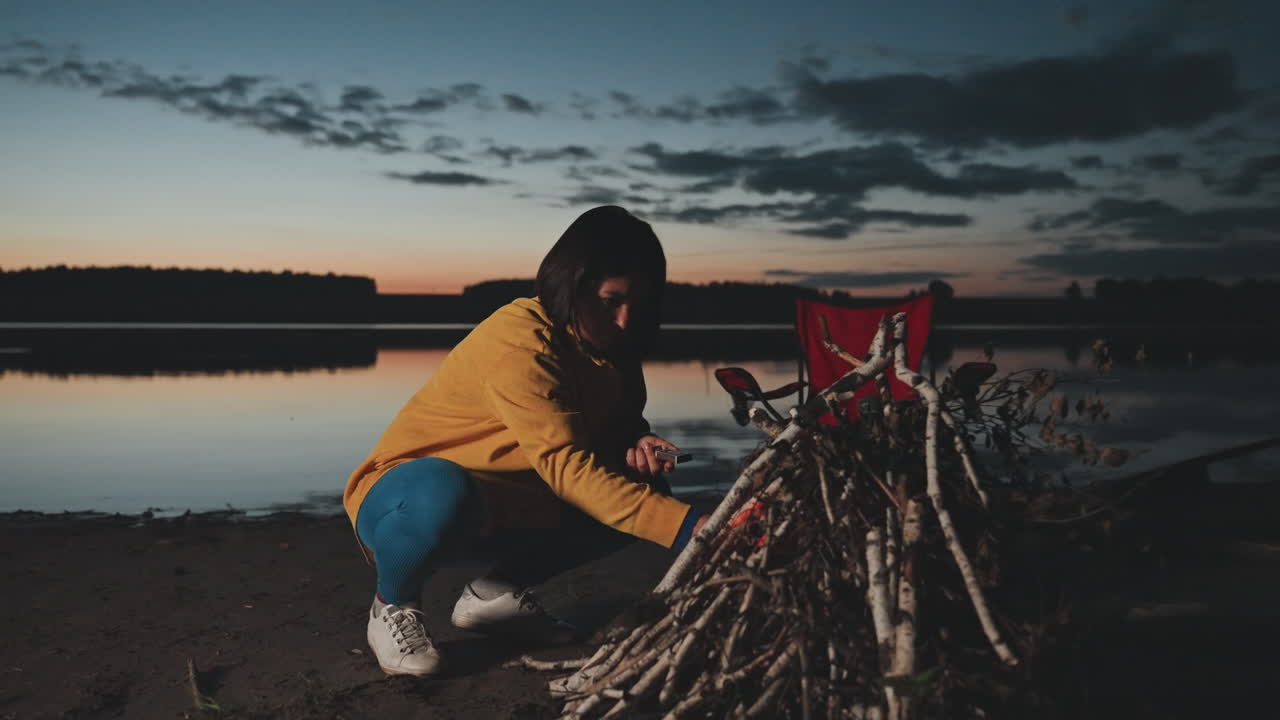 Campfire glow illuminates peaceful lakeside scene. Serene evening next to calm water with gentle campfire light. Intimate camping experience with flickering fire and reflective water in quiet night