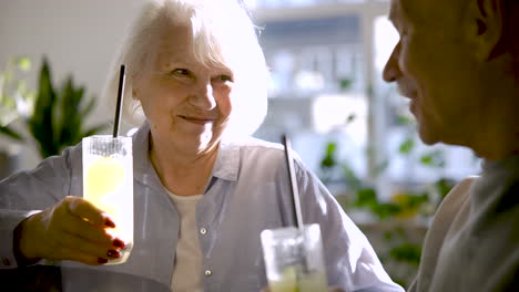 Close-up-view-of-a-senior-couple-drinking-limonade-and-laughing-while-they-are-sitting-in-a-bar-at-sunset