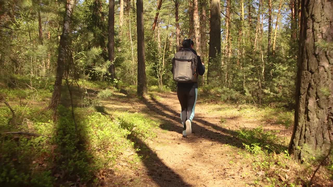 mujer caminando con una mochila de senderismo en el bosque verde de primavera
