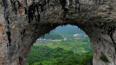 Drone-approaching-natural-arch-of-Moon-Hill-with-stalactites-in-Yangshuo,-China