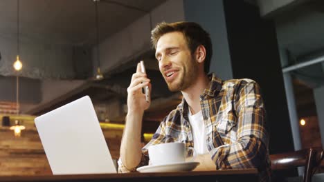 man talking on mobile phone while using laptop in cafe 4k