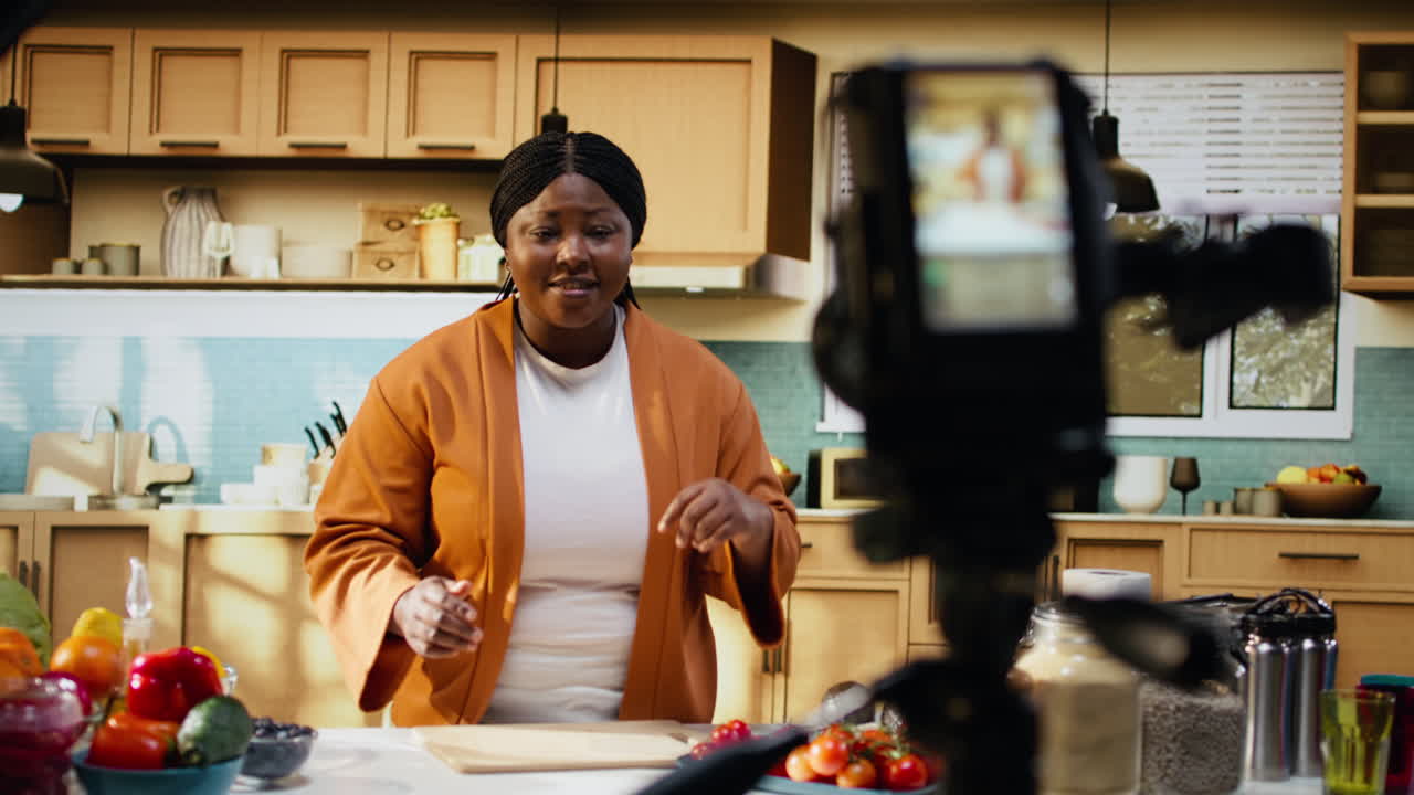 Vlogger di cucina (donna di colore) filma contenuti culinari con treppiede e telecamera