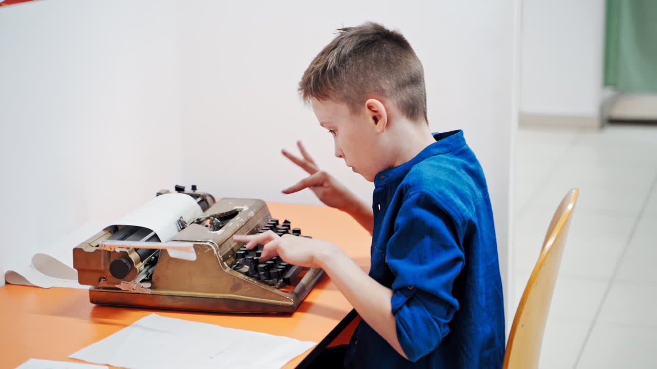 Boy sitting at table and typing old typewriter.