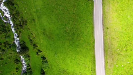 Vehicles-travelling-along-a-road-between-two-fields-of-grass,-aerial