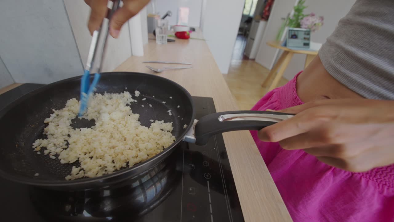 Person stirring rice in a pan on a stove