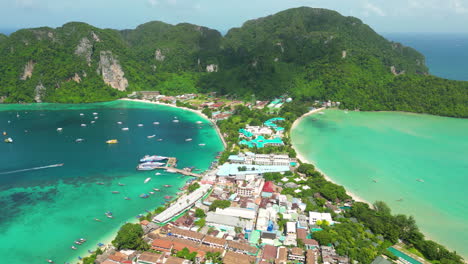 Aerial-tilt-down-shot-of-Phi-Phi-Island-with-many-boats-on-clear-bay-water-and-hotel-resorts-during-summer-season-in-Thailand,Asia