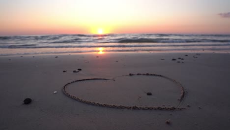 símbolo de corazón dibujado en la arena contra un telón de fondo de puesta de sol sobre el mar