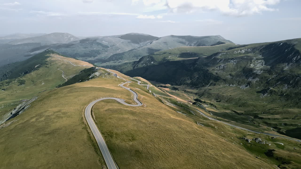 vista panorámica de la carretera transalpina en rumania, con terrenos ondulados y paisajes contrastantes bajo un cielo nublado