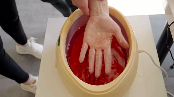 Beauty salon, a cosmetologist immerses the client's hand in paraffin