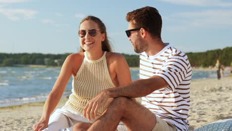 pareja feliz con la comida haciendo picnic en la playa. ocio, relaciones y personas concepto pareja feliz con los alimentos comiendo uvas y haciendo picnicen la playa