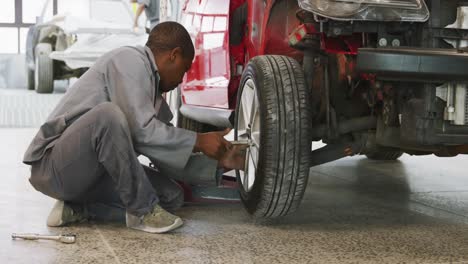 mecánico de automóviles afroamericano atornillando una rueda a un automóvil con una llave inglesa