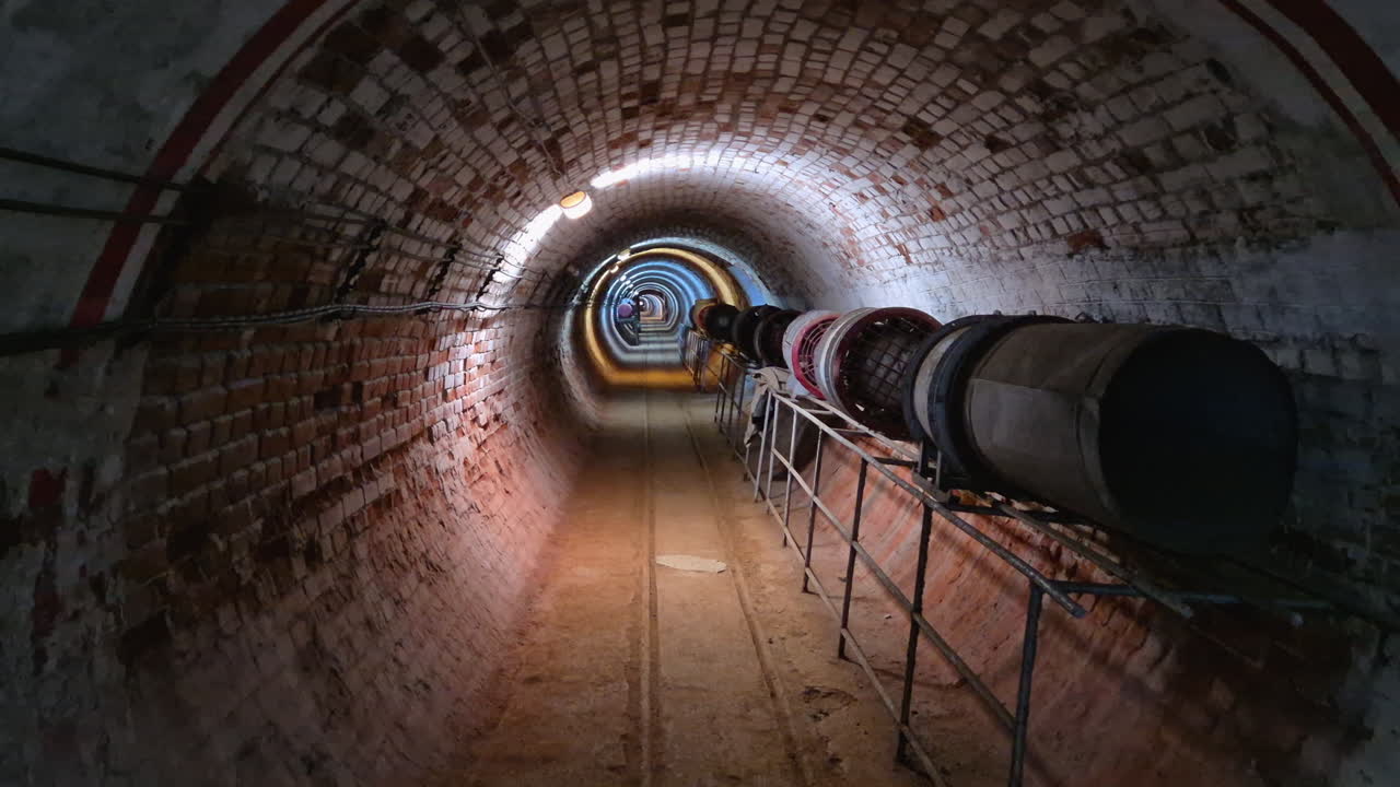 Inside a long straight underground mine tunnel with ventilation pipes, tilt up, The Museum of Mining in Pernik, Bulgaria