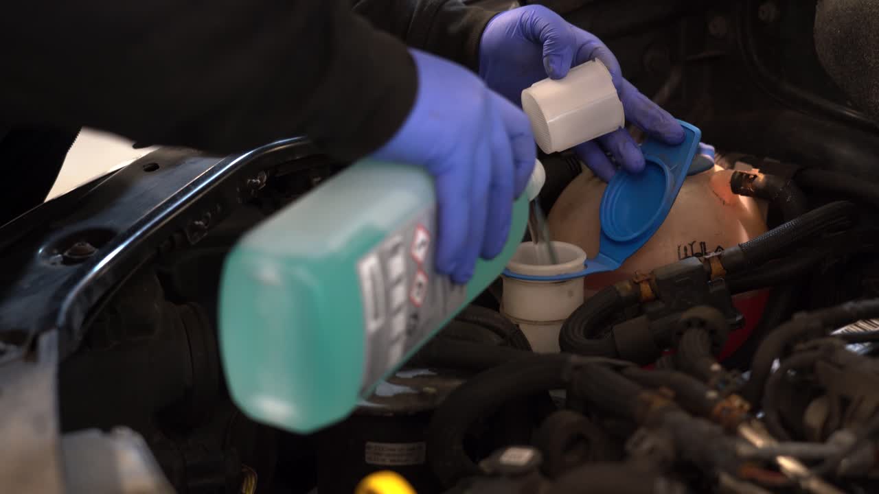 A technician fills a vehicle washer bottle (no logos only COSHH symbols)