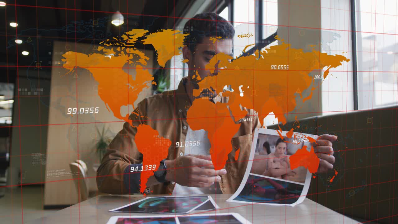 Man holding up print and presenting designs at cafe table, orange world-map overlay aligning