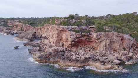 Flying-around-cliffs-at-S'Almonia-beach-Mallorca-during-a-cloudy-day,-aerial