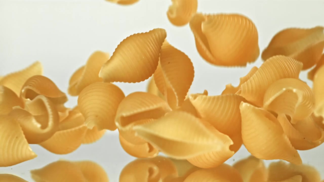 Pasta conchiglie secca che cade al rallentatore su una superficie bianca
