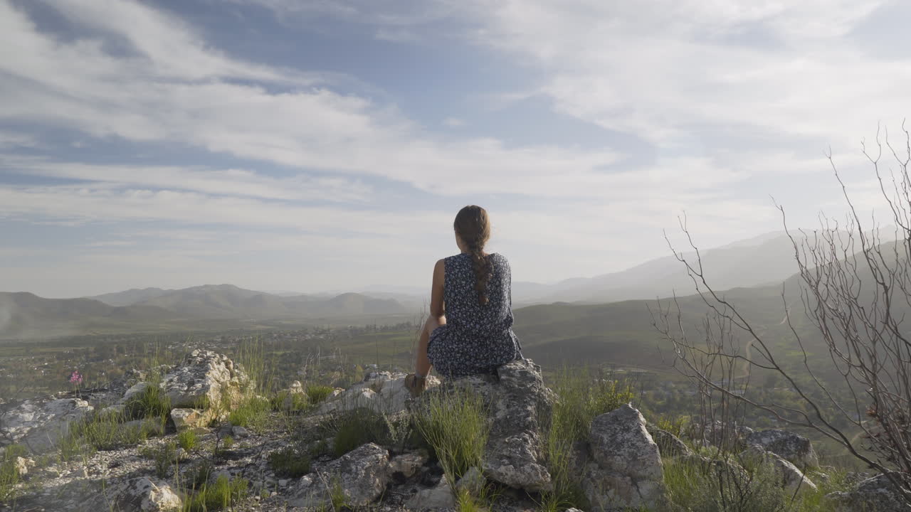 la chica se sienta en lo alto de una montaña mirando hacia abajo en una ciudad rural