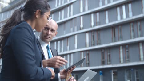 side view of business colleagues watching and discussing content on tablet outside