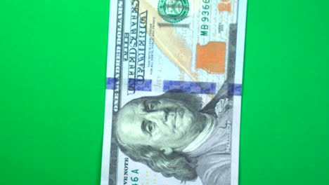 one hundred dollars slowly spinning on a rotating green background.