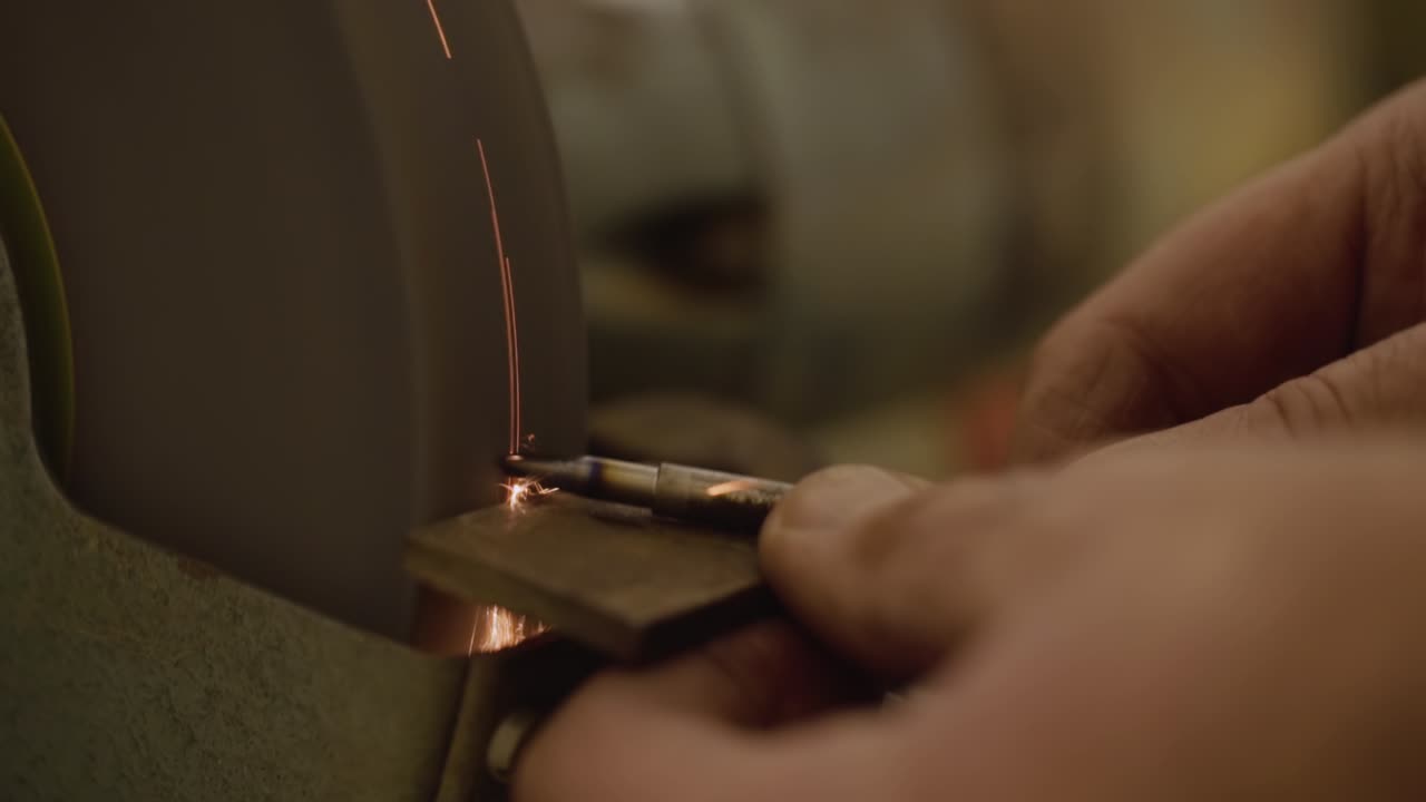 herrero usando una máquina de molienda con piedra de afilar para formar una herramienta metálica, chispas volando hacia la cámara en cámara lenta macro de primer plano