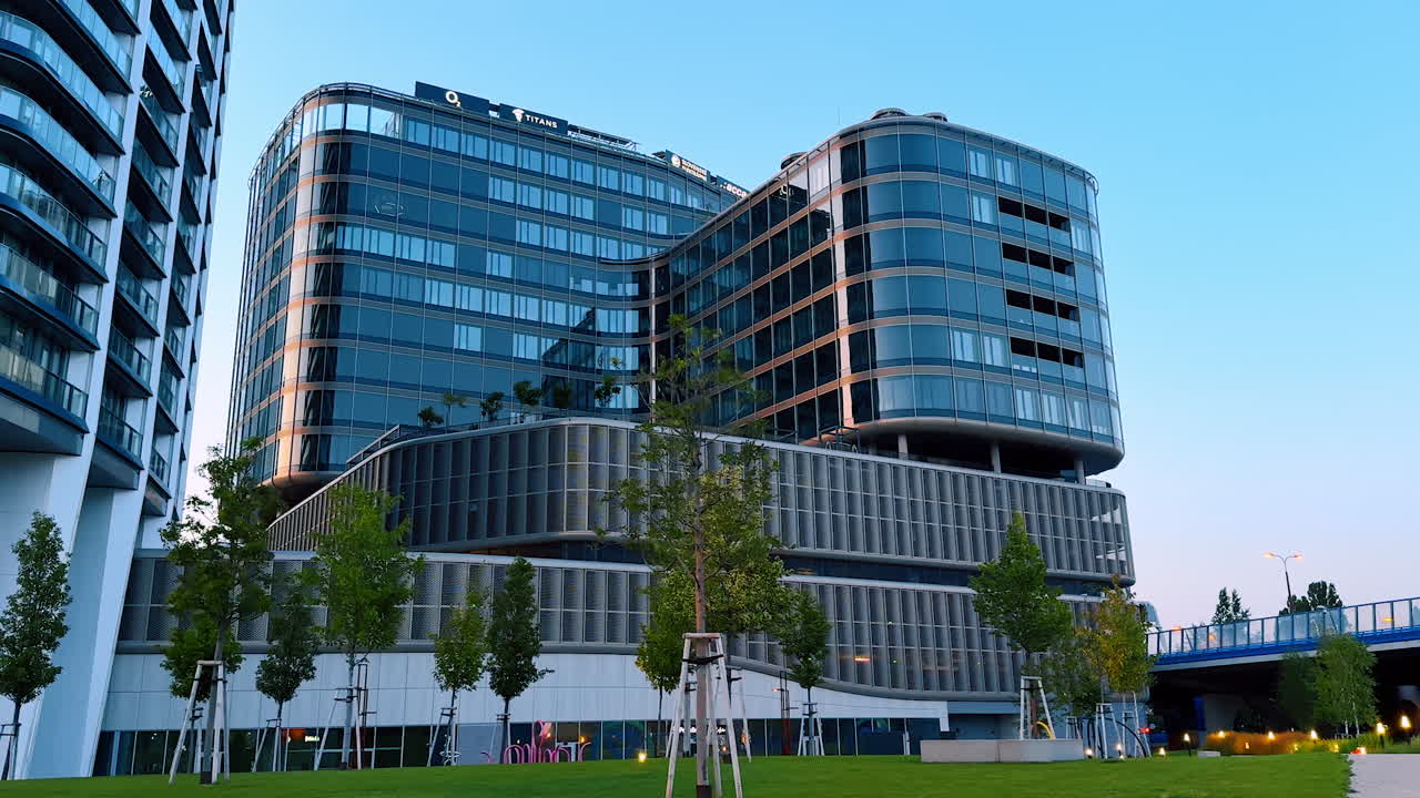 Bratislava, Slovakia - June 5, 2025: Modern office building in urban setting. A sleek office structure with glass exterior stands in a green area, showcasing contemporary architecture during dusk
