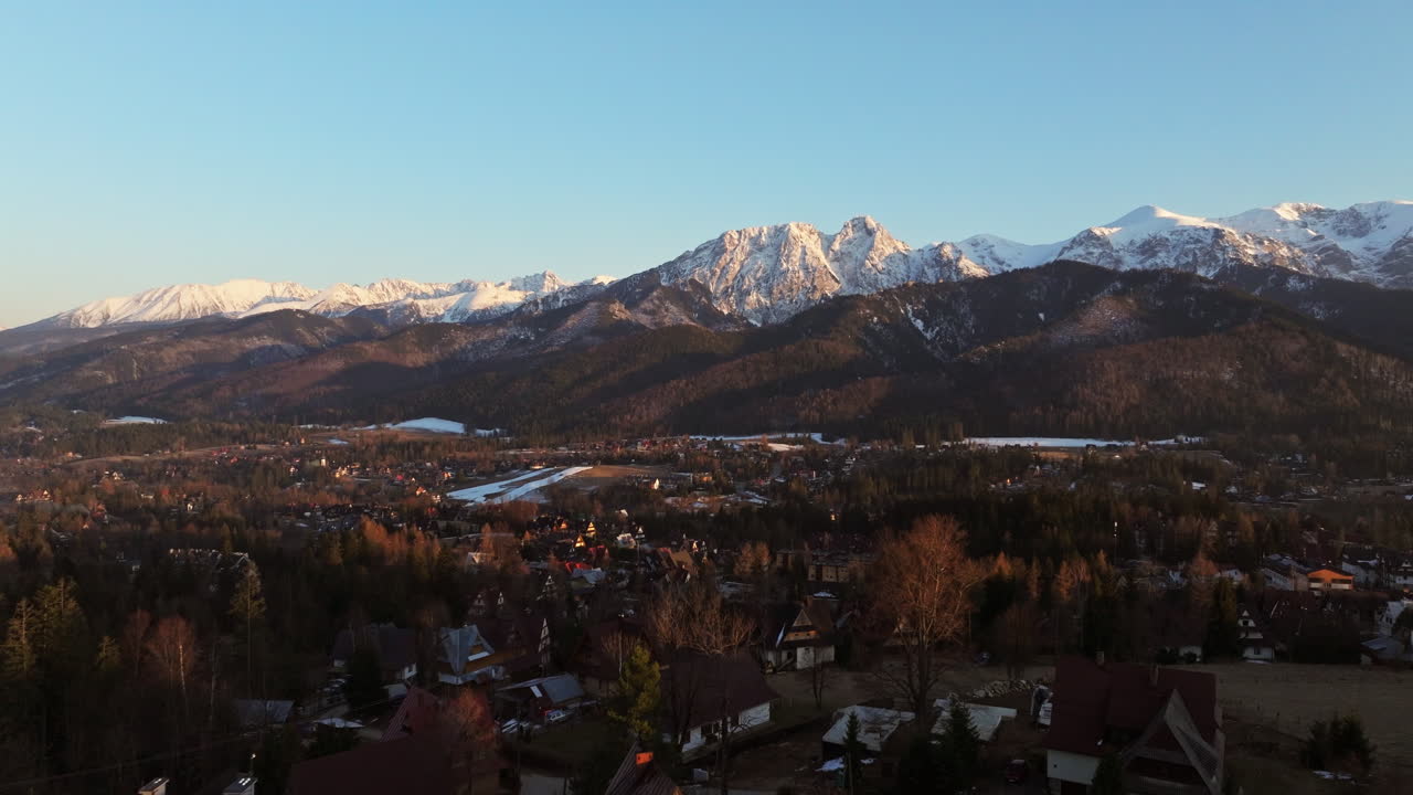 Mountain terrain glows under golden hour light with distant hills and forests visible, quiet mountain town in foreground