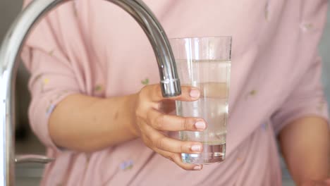 woman filling glass with water from kitchen tap