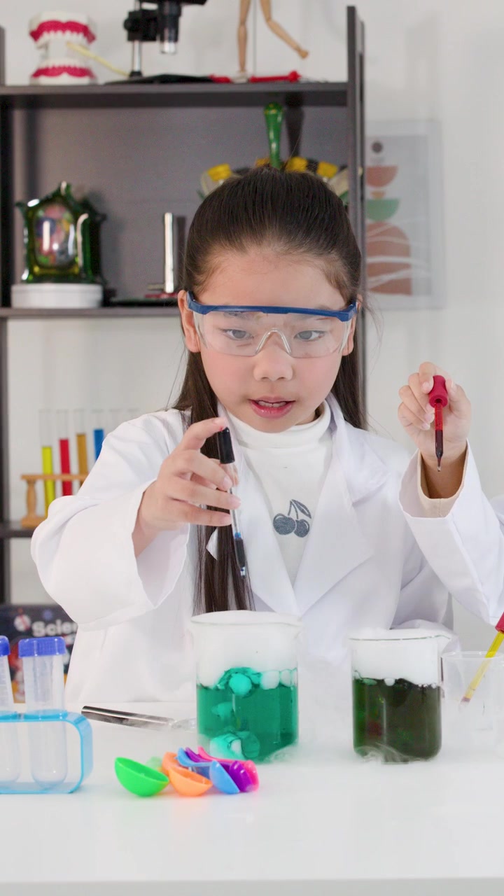 Seorang gadis muda mengenakan kacamata pengaman menggunakan pipet untuk percobaan kimia di dalam kelas.