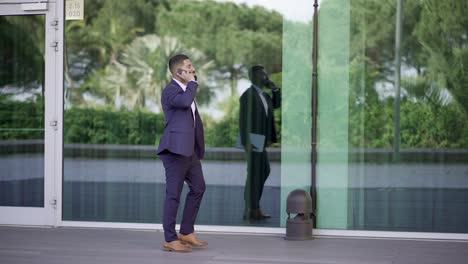 Businessman-holding-laptop-and-talking-by-cell-phone-outdoor