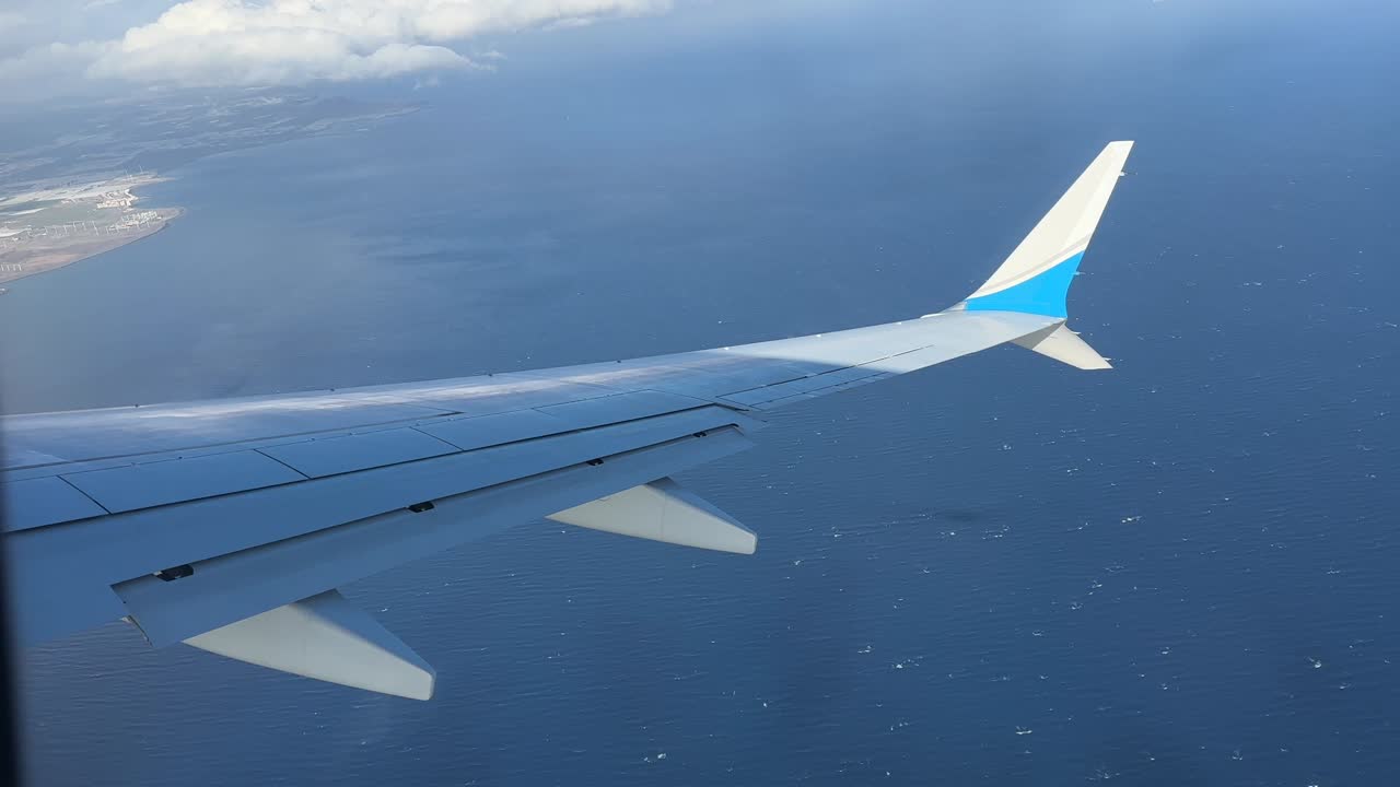 Asa de um Boeing 737 Max vista da janela de um passageiro durante uma curva suave sobre a água, ao se aproximar do Aeroporto de Gran Canaria, filmagem aérea tranquila.