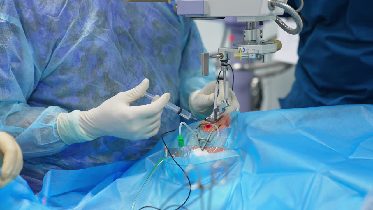 Surgeon's gloved hand holds the syringe inputting medicines into patient's eye. Doctor holding device tool in another hand.