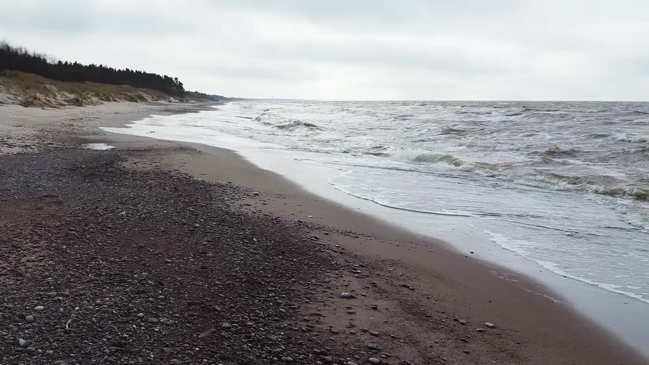 Aerial low altitude flyover view of sea waves crashing into the beach in overcast spring day, Baltic sea, Nida beach, Latvia, wide angle drone shot moving backwards
