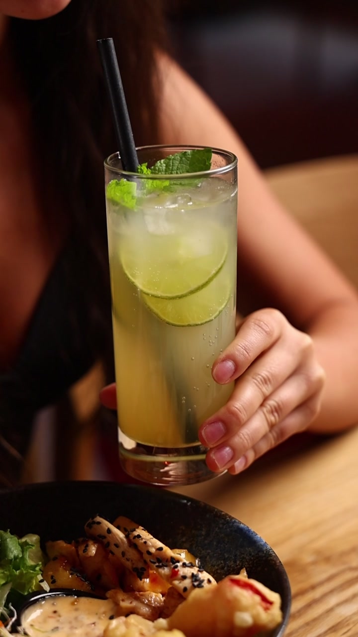 Donna che tiene in mano un rinfrescante cocktail al lime e menta in un ristorante