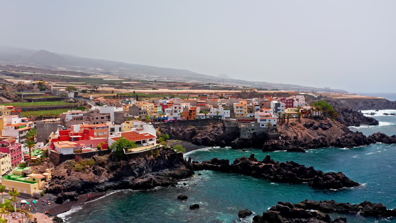 Aerial drone shot over the beautiful volcanic rocky coastline of Tenerife, Canary Islands, Spain. High view of the turquoise sea volcanic coast and the local towns. Summer holidays destination.