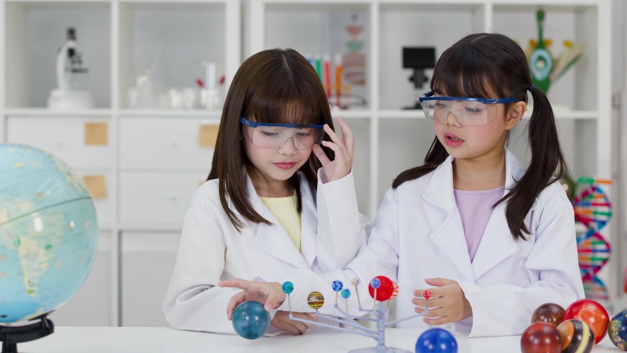 Nuoret opiskelijat laboratoriotakeissa tutkivat planeettamallia tiedetunnin aikana sisätiloissa.