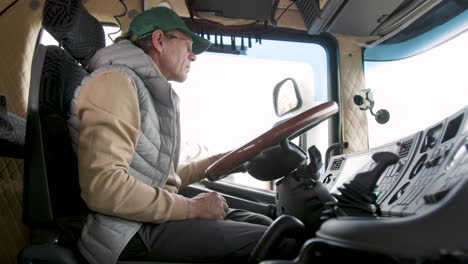 side view of older worker wearing cap and vest driving a truck in a logistics park 5