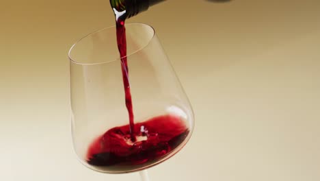 red wine pouring into glass over yellow background with copy space