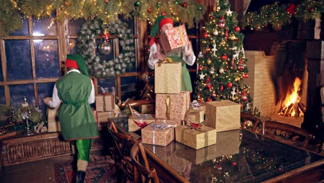 happy elves with many presents indoors. christmas decorated room and elves in green costumes putting packed gifts on the table. christmas time.