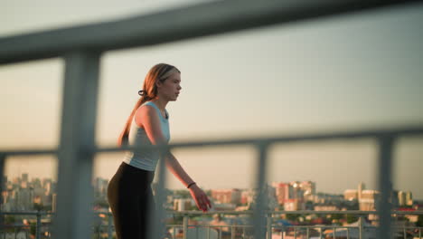 young lady roller skating outdoors, with focus on iron railing in foreground, cityscape with buildings and sunset glow is visible in blurred background