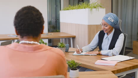 moslim zakenvrouw die aantekeningen maakt terwijl ze op tafel zit, vergezeld van haar collega's