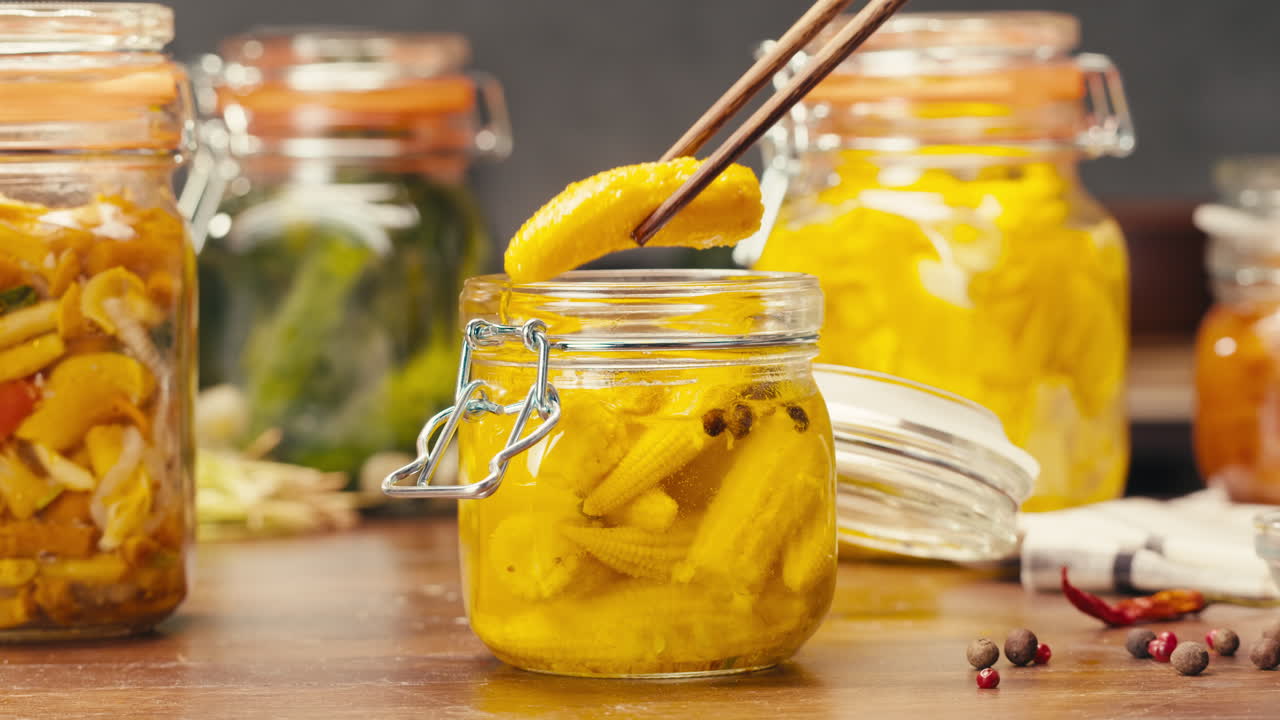 Fermented food in glass cans on table close-up. Preservation of vegetables in glass jars. Fermentation preserved mini corns, kimchi, cucumbers, mushrooms with spices.