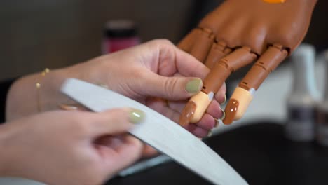 la manicura crea la forma correcta de las uñas en una mano protésica con una lima de uñas.