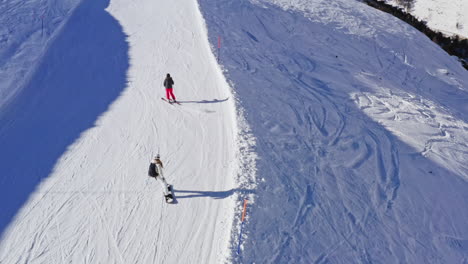 Toma-Aérea-Siguiente-Para-Esquiador-Y-Snowboarder-Bajando-La-Pendiente-Nevada